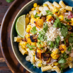 Elote pasta salad garnished with Cotija cheese and lime.