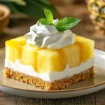 A close-up of Pineapple Pretzel Salad squares on a plate, showing layers of crunchy pretzel crust, creamy filling, and pineapple Jell-O topping, garnished with whipped topping and mint.